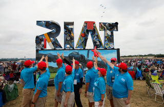 CREW standing and pointing at the RIAT25 sign.