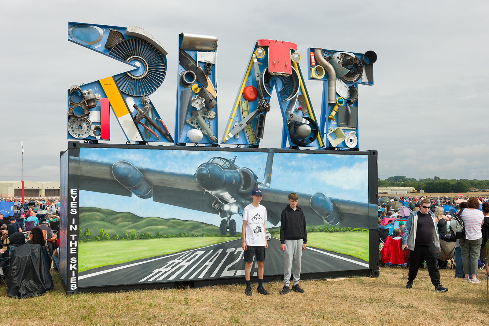 Two young men standing in front of the RIAT sculpture at RIAT25.
