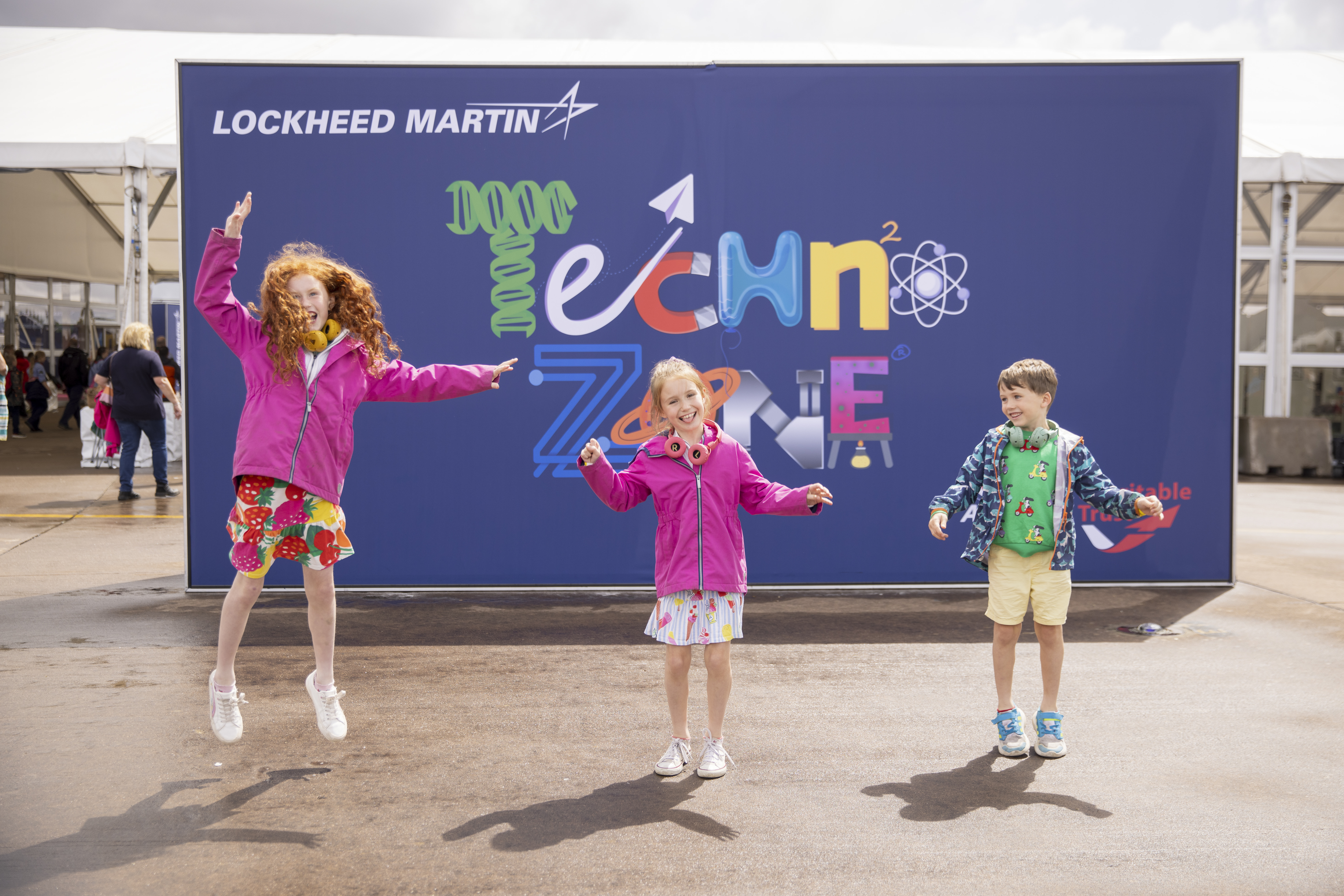 Girl jumping in front of the Techno Zone sign with a girl and a boy.