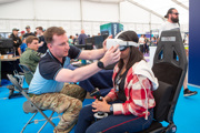 Young girl wearing a virtual reality headset with goggles being adjusted by a man in the Techno Zone at RIAT24.