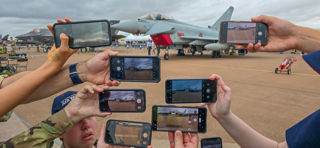 Hands holding smart phones to take picture of static aircraft at RIAT24